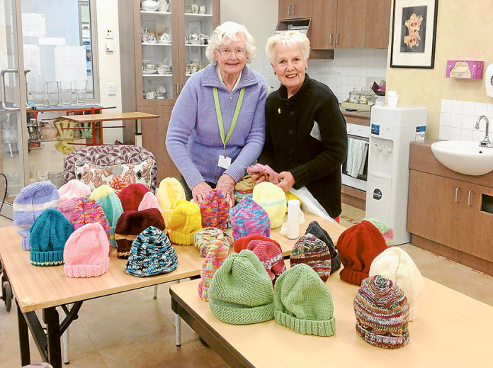 HELPING THE WHOLE COMMUNITY… From left, Banksia Lodge volunteer, Beryl Granger and GV Health volunteer, Faye Todd with the knitted beanies that the Shepparton Villages Banksia ladies knitted for the oncology unit at GV Health. Photo: Supplied.